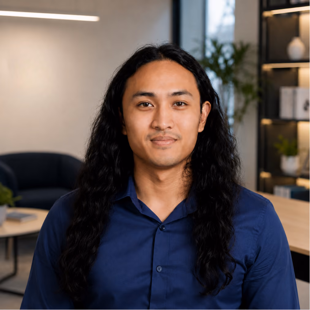 Portrait of a smiling ClinicSense team member with long hair wearing a blue shirt in a modern office.