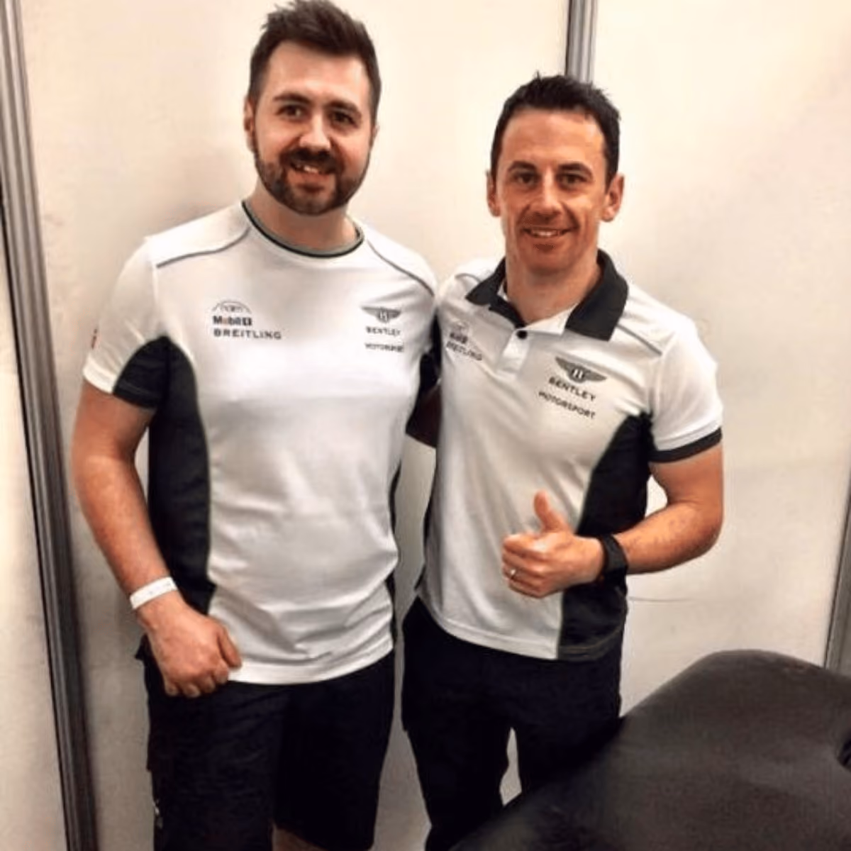 Two men in Bentley Motorsport shirts standing side by side, one giving a thumbs up.