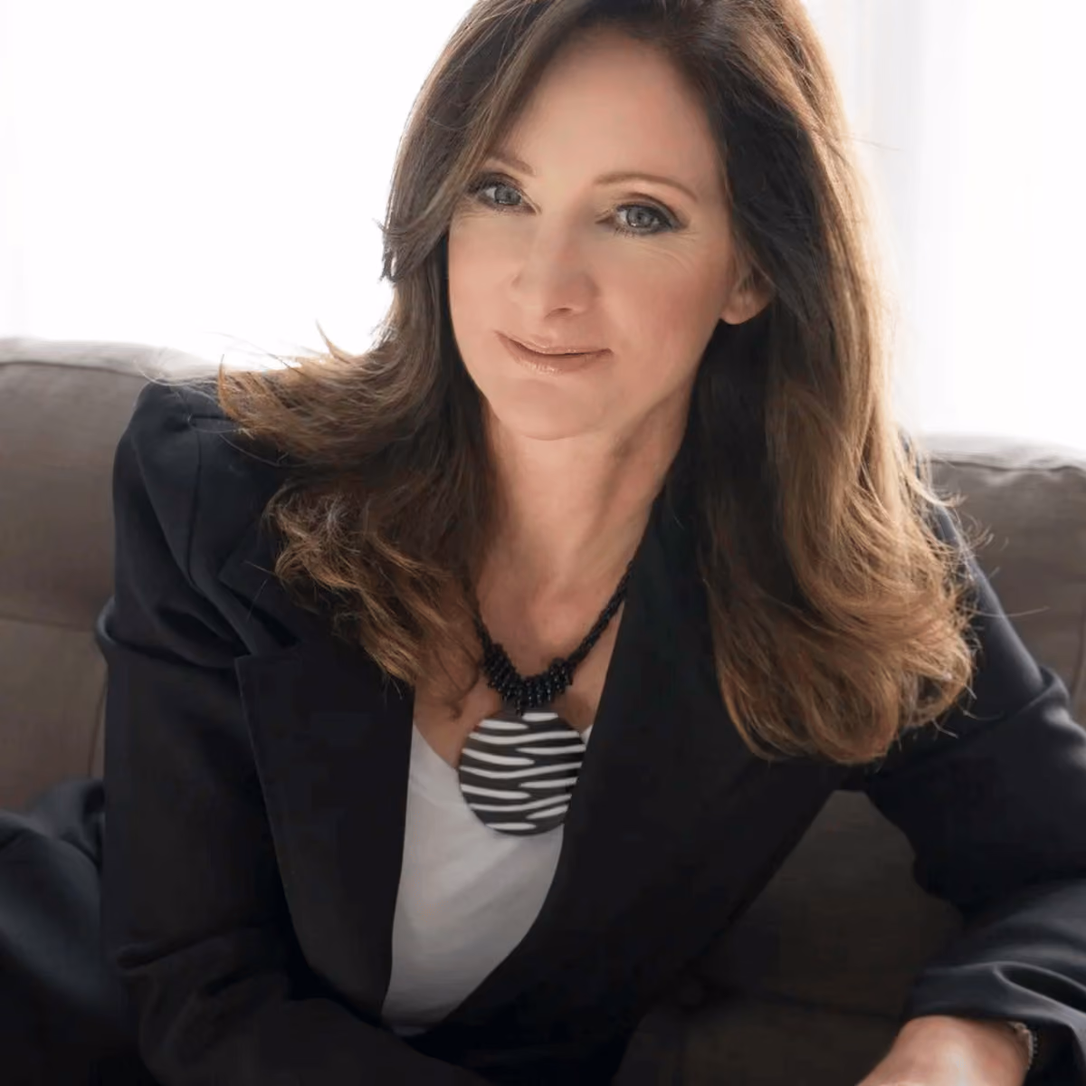Smiling woman with brown hair wearing a black blazer and black-and-white patterned necklace.