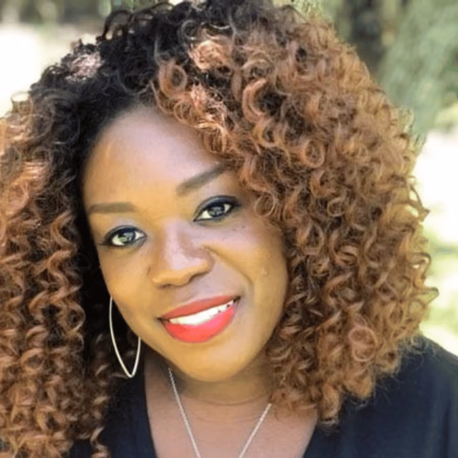 Close-up of a smiling woman with curly brown hair, red lipstick, and hoop earrings.