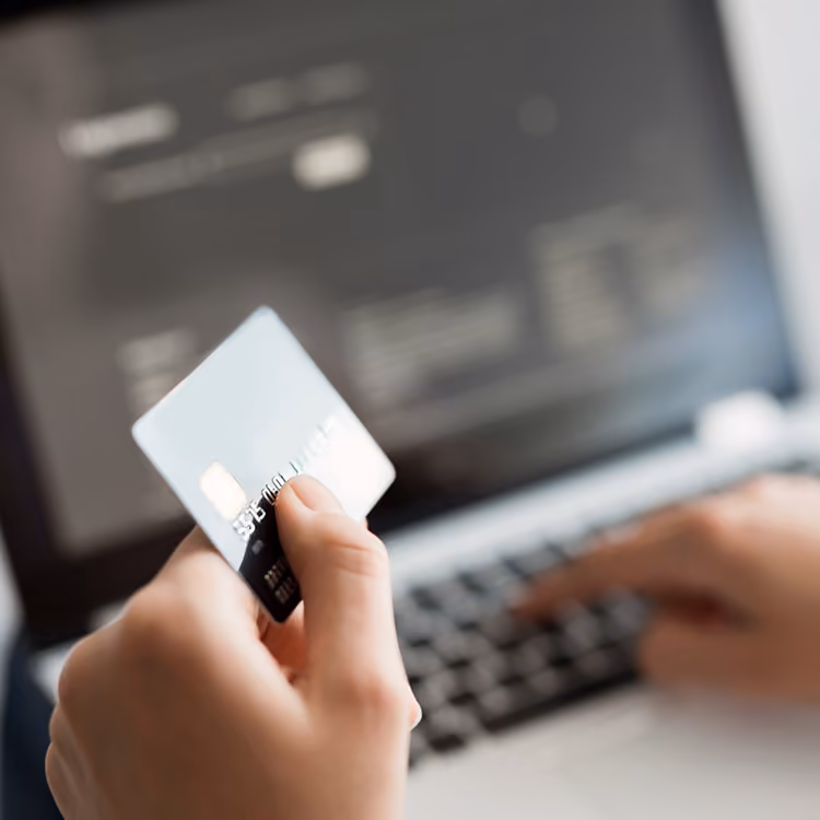 Person holding a credit card in one hand while typing on a laptop keyboard, suggesting online payment or shopping.