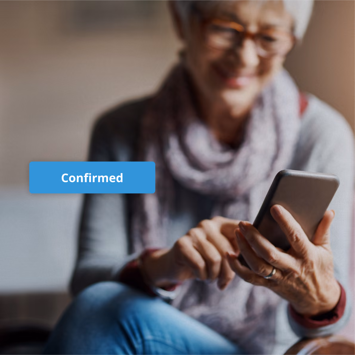 Elderly woman wearing glasses and a scarf, smiling while using a smartphone, with a blue label reading 'Confirmed' beside her.