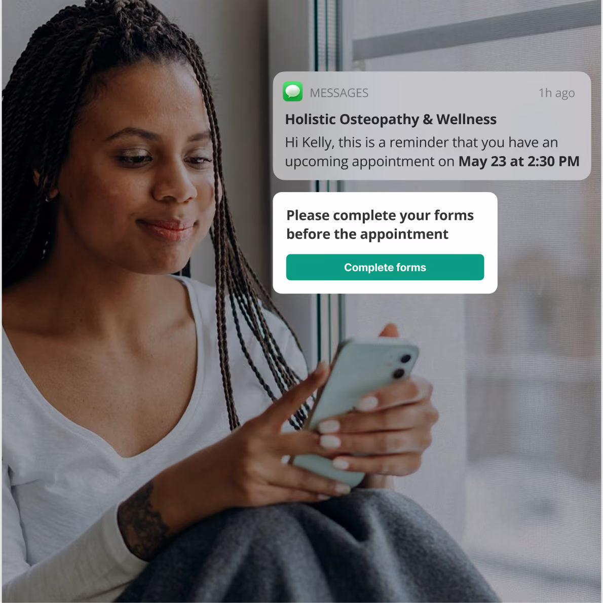 Smiling woman with braided hair sitting by a window, holding a smartphone, with an on-screen message reminder about an upcoming appointment on May 23 at 2:30 PM and a prompt to complete forms before the appointment.