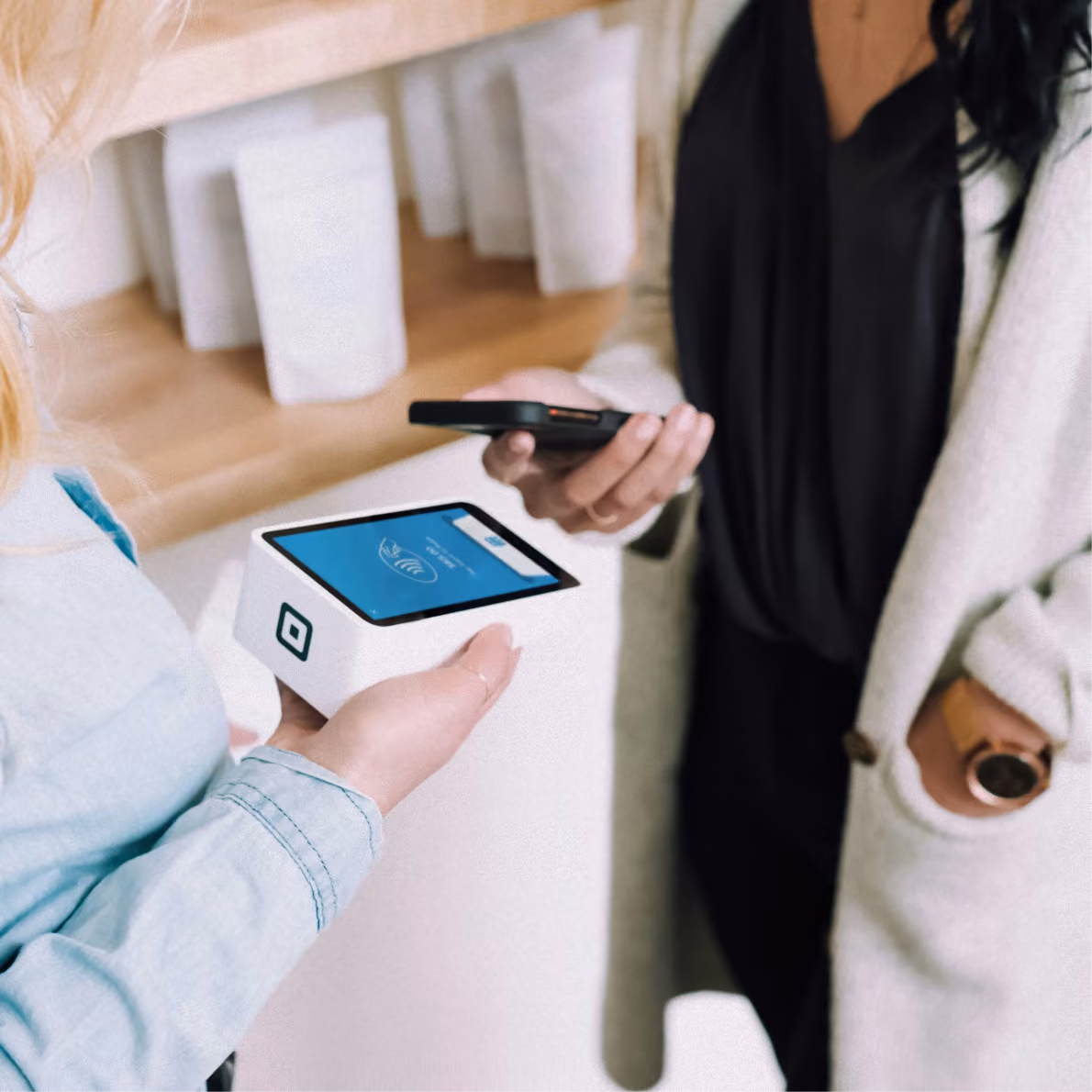 Client tapping a phone on a Square card terminal held by a staff member to pay.