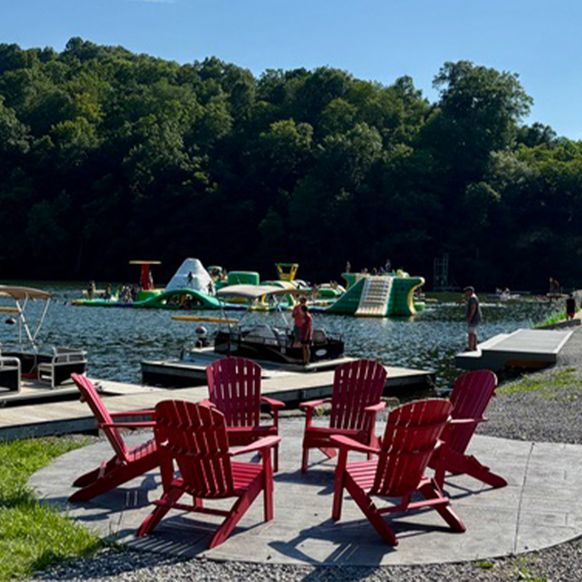 A campground with chairs around a fire near a lake