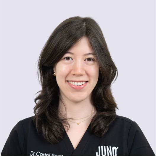 Dr. Corini Ross smiling in black Juno veterinary scrubs against a light purple background