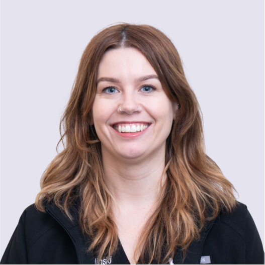 Dr. Sarah smiling in a black zip-up top, long auburn hair.