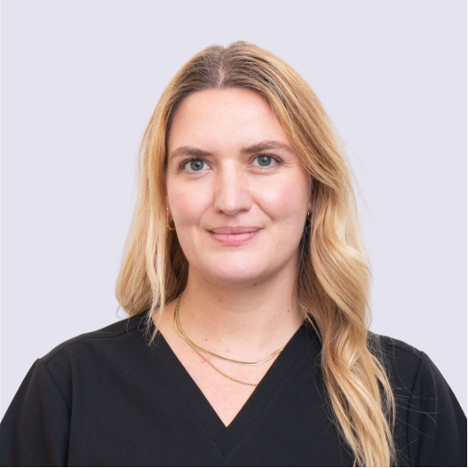 Dr. Esther smiling in black scrubs and layered gold necklaces, long blonde wavy hair.