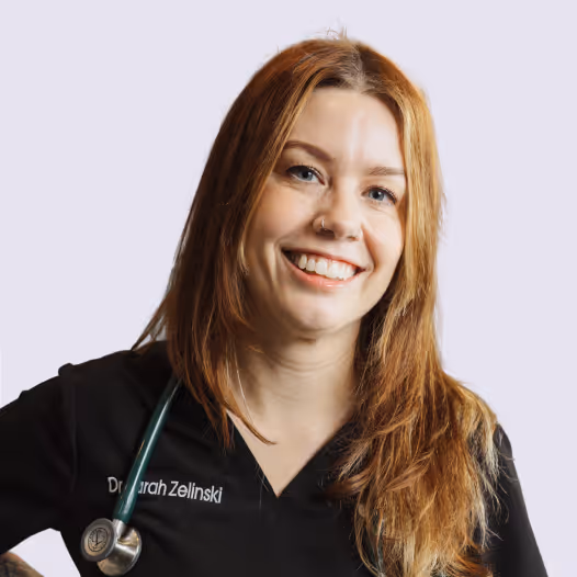 Dr. Sarah has long red hair and is wearing black scrubs and a stethoscope around her neck