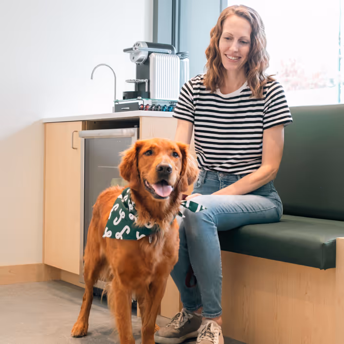Smiling pet owner sitting with a golden retriever wearing a green Juno Veterinary bandana in an exam room