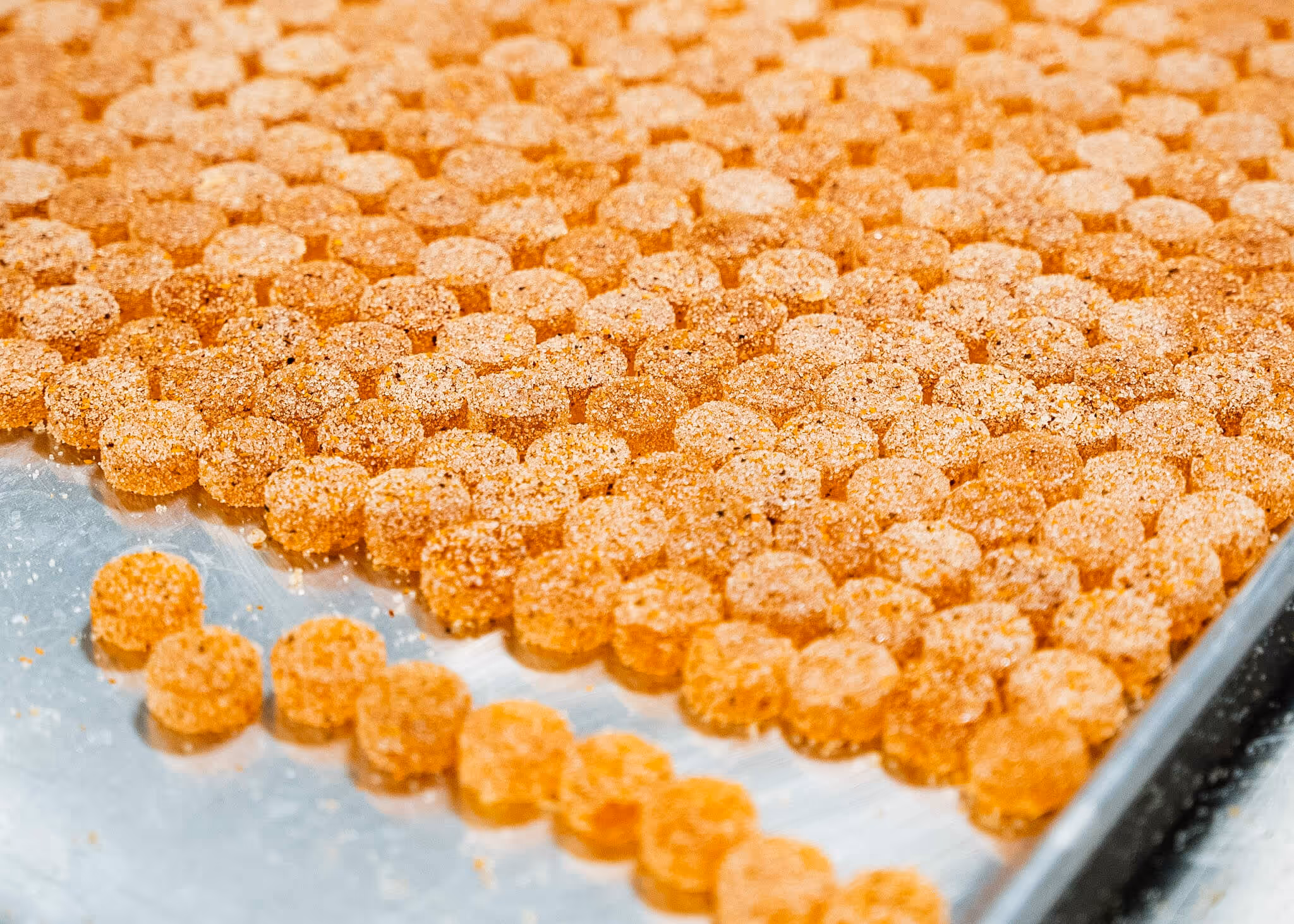 Rows of small, round orange gummy candies coated in sugar on a metal tray.