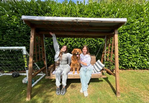 Two girls sitting on garden swing with brown dog