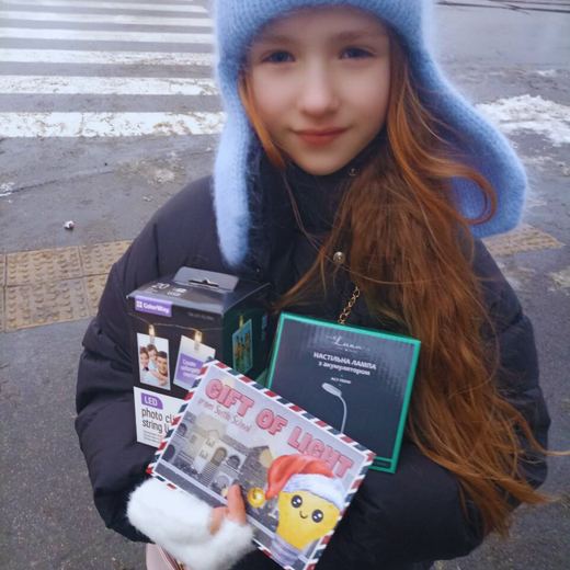 A student in a winter hat holding a desk lamp and photo string lights