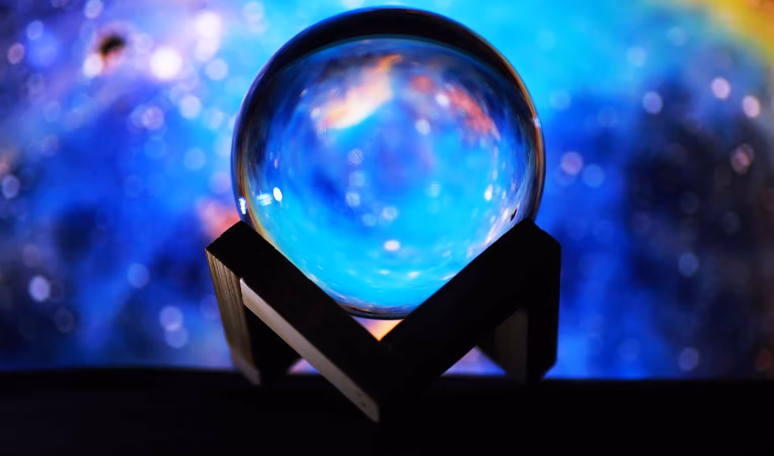 Leuchtend blaue Kristallkugel auf dunkler Halterung vor unscharfem, galaxieähnlichem Hintergrund – Symbol für Zukunftsblick/Prognosen.