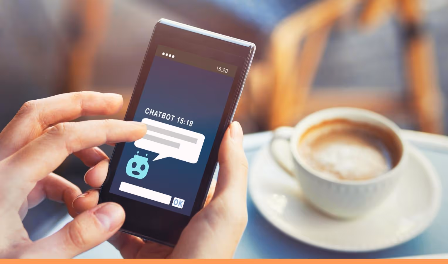 Nahaufnahme: Hände tippen auf ein Smartphone mit Chatbot-Chatfenster auf dem Display; im Hintergrund steht unscharf eine Tasse Kaffee auf Unterteller.