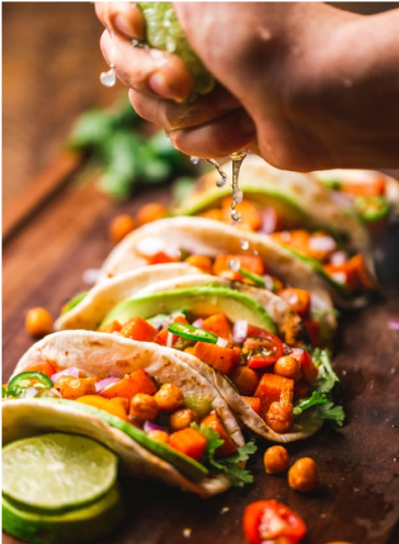 A hand squeezing lime juice onto several tacos.