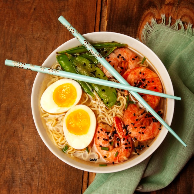 A bowl of spicy shrimp ramen with chop sticks laying on top.