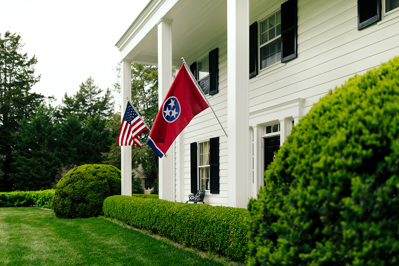 Healthy lawn and boxwoods beside a white porch with a Tennessee flag