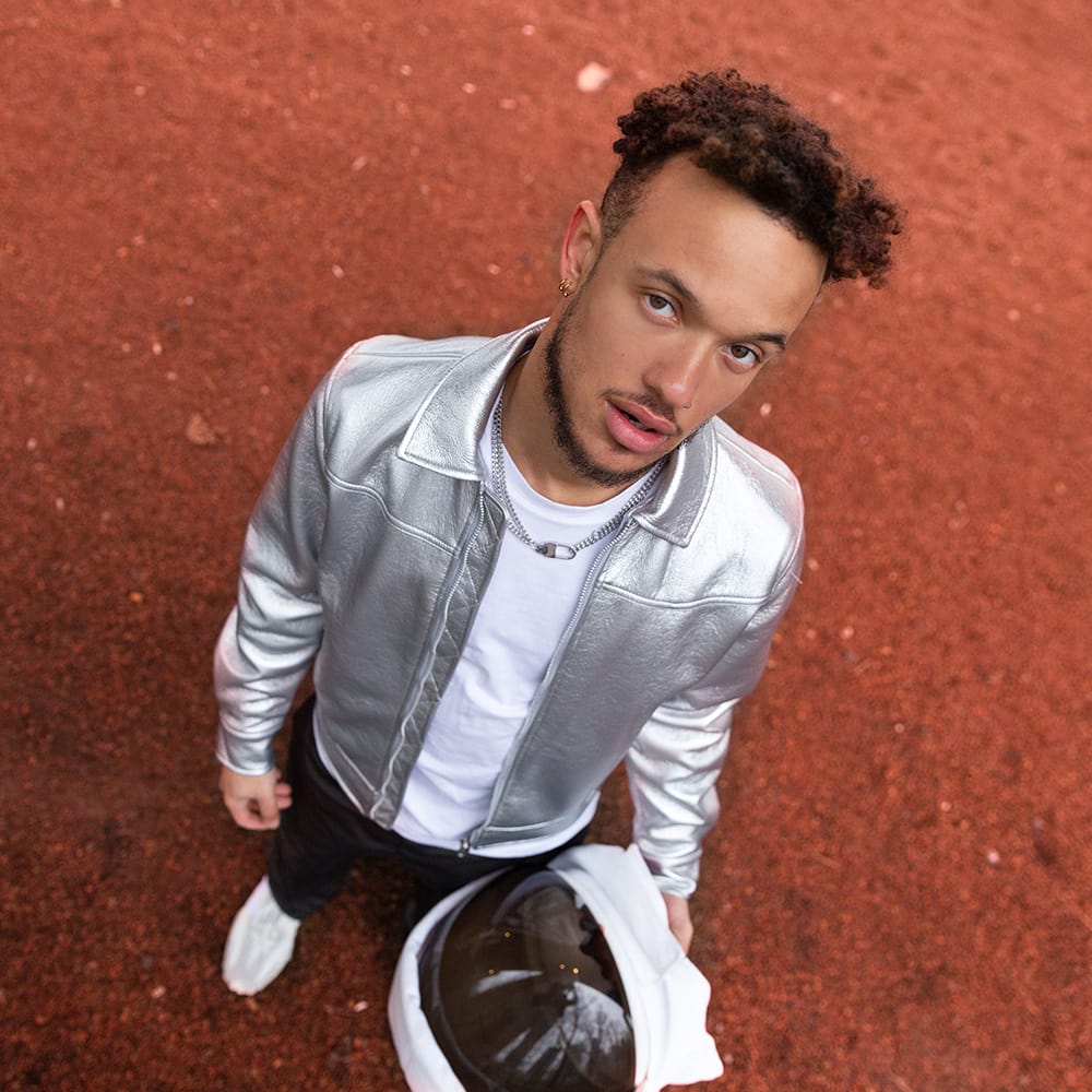 Vincent Darby looking to the sky wearing a silver jacket and holding a white astronaut helmet on a tarmac  ground