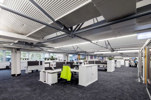 The interior of a commercial building. There are open plan desks in a large warehouse style room