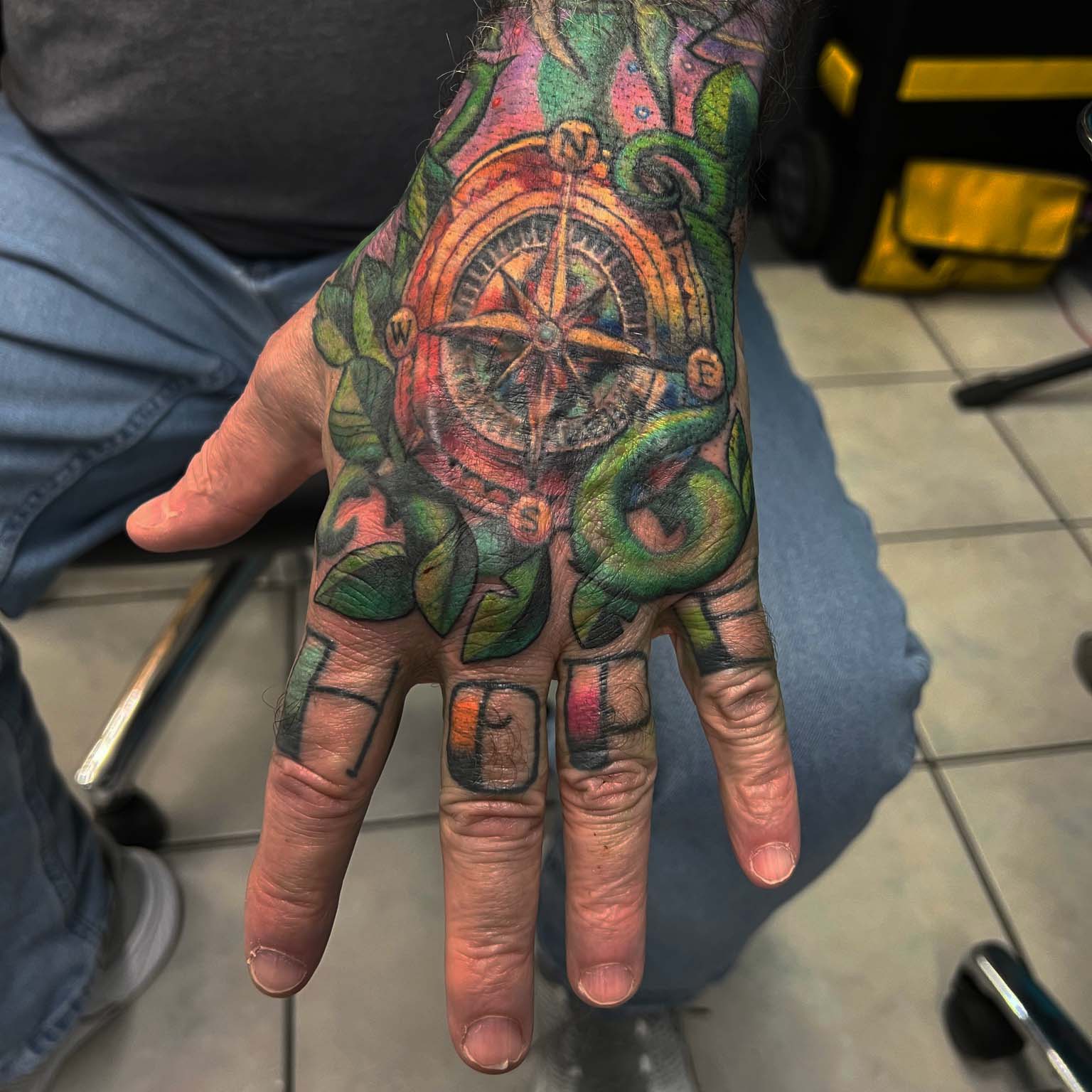 Color compass hand tattoo with vines and green leaves