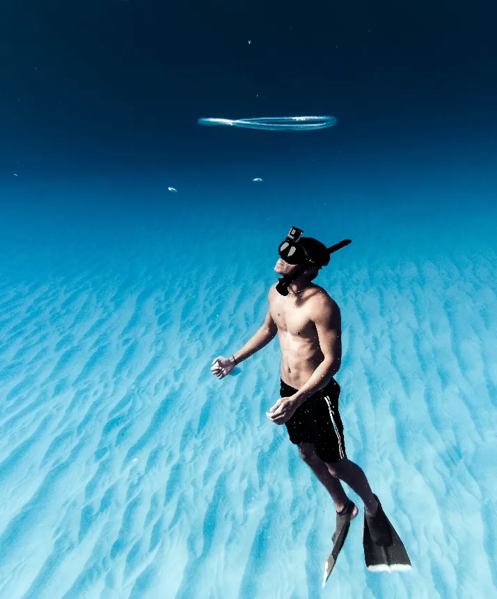 A male diver in crystal clear waters going to the surface.