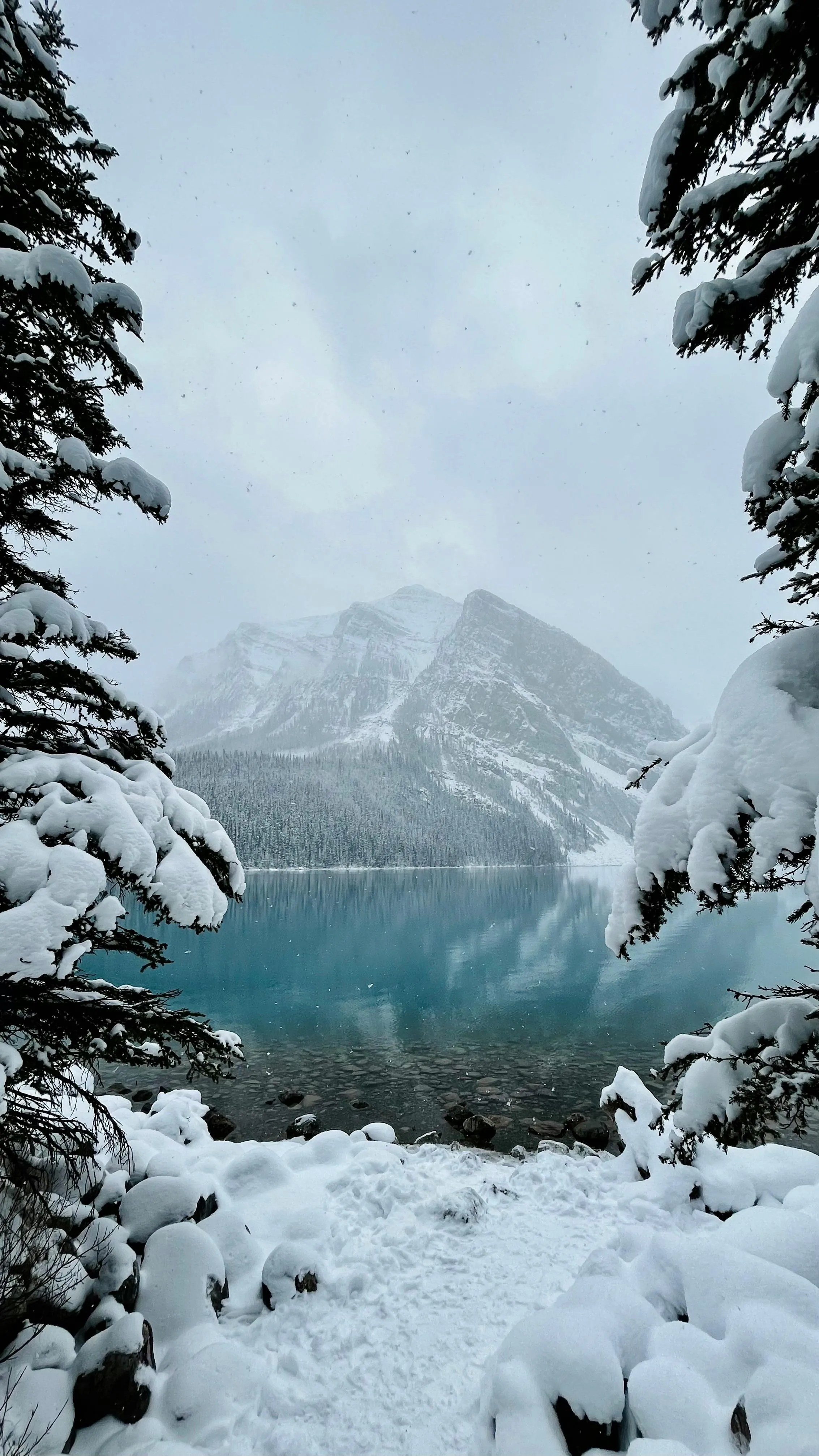 A lake near a mountain in Canada and the surrounding terrain is covered in snow.