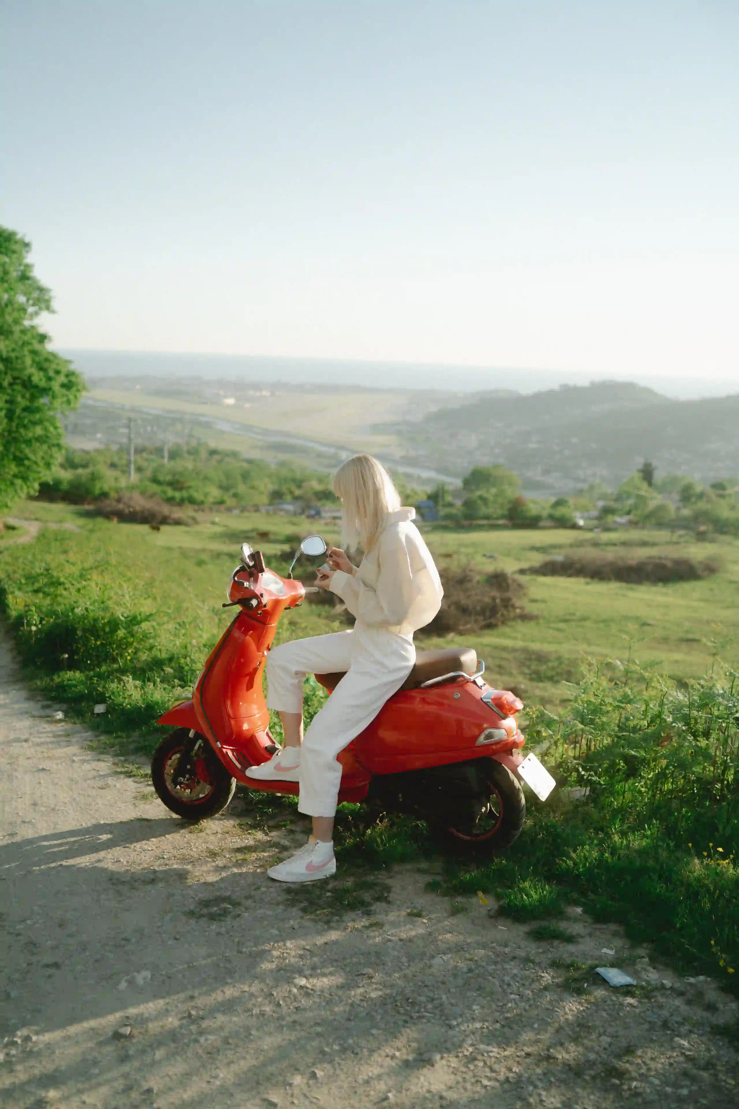 A young lady on a red scooter in France while in a green tranquil environment.