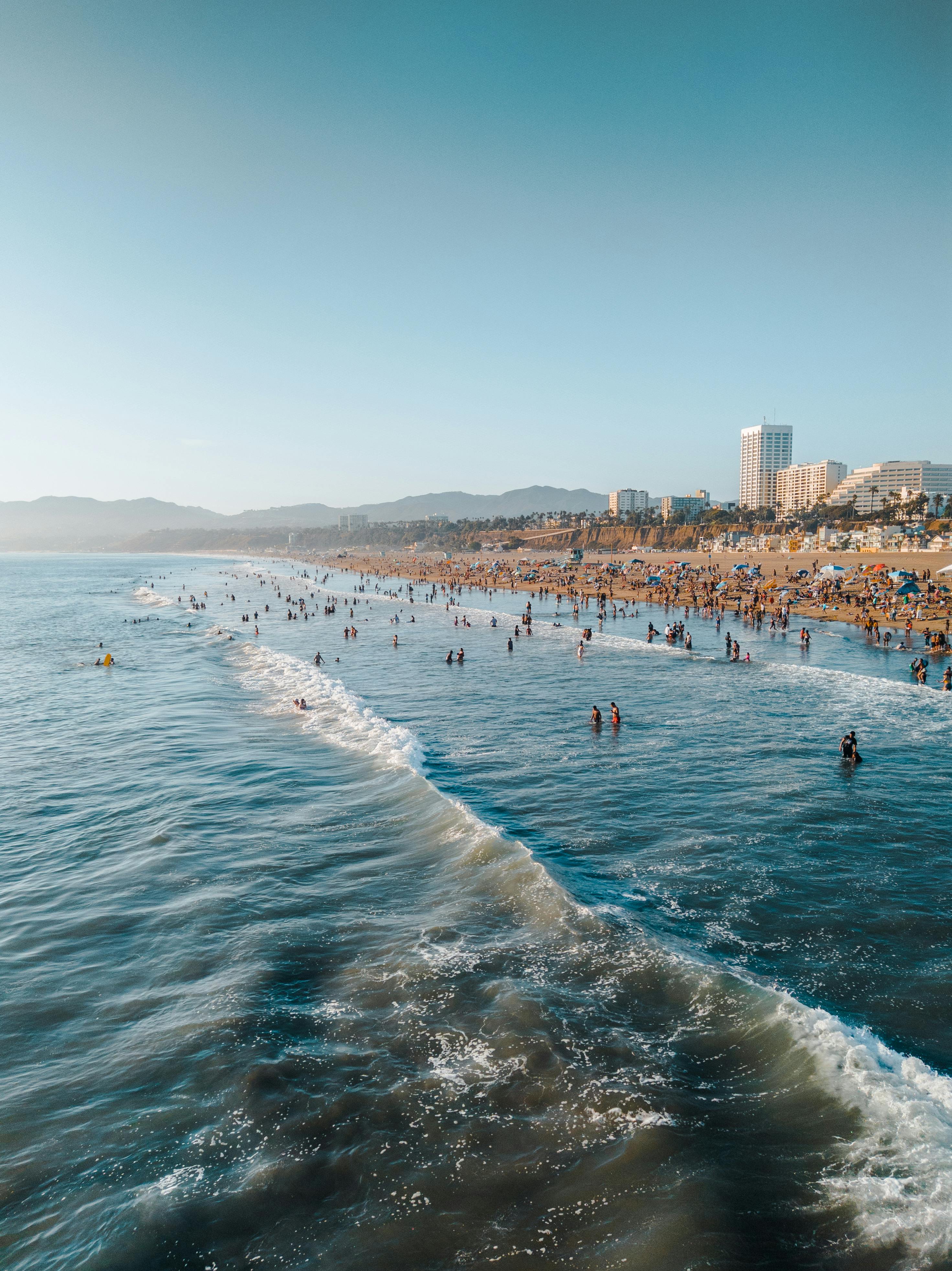 Beach of Los Angeles while people swim in the sea and a wave is coming to the shore.