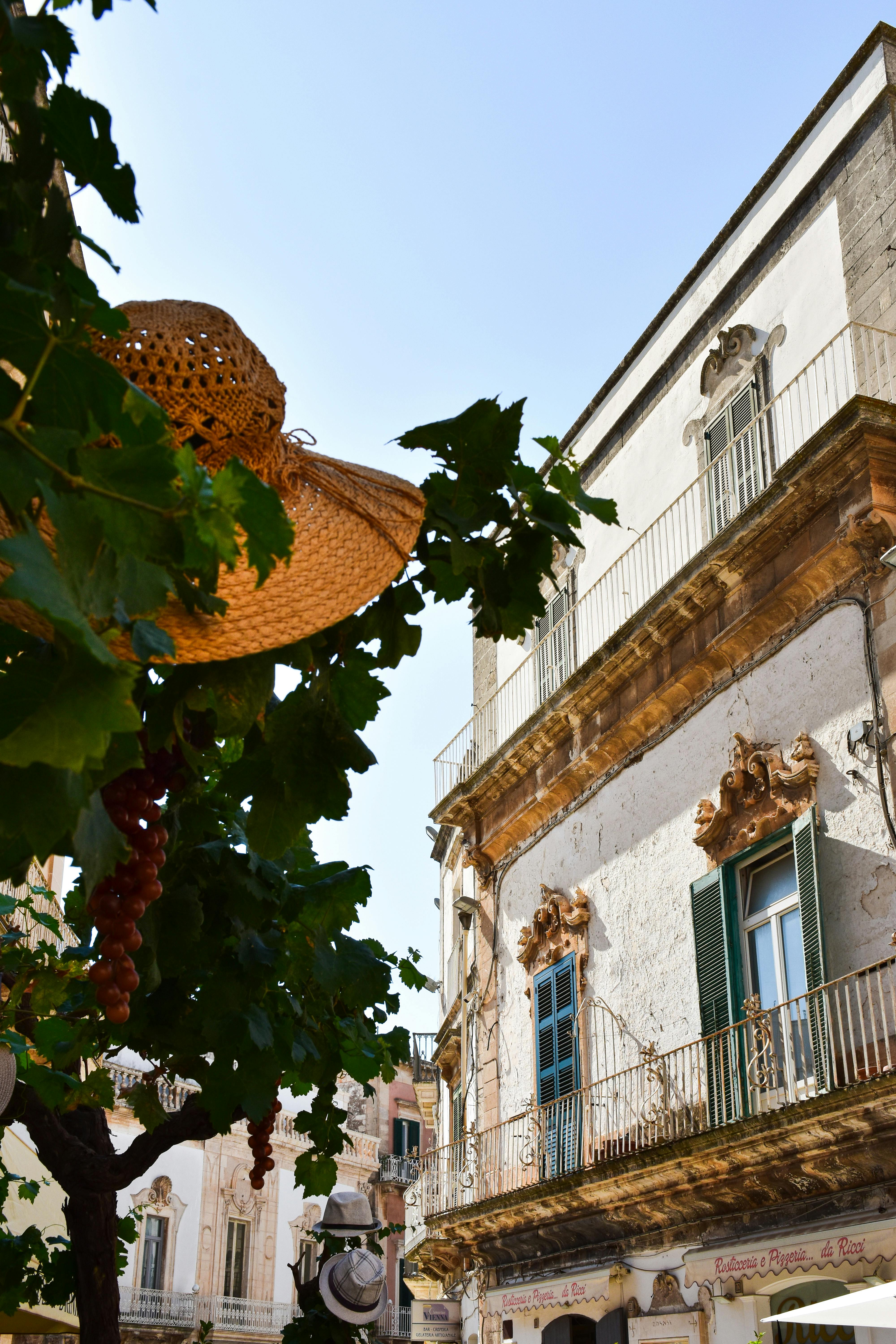 A street in a town in Puglia with a white characteristic house in the background and a straw hat in the trees.