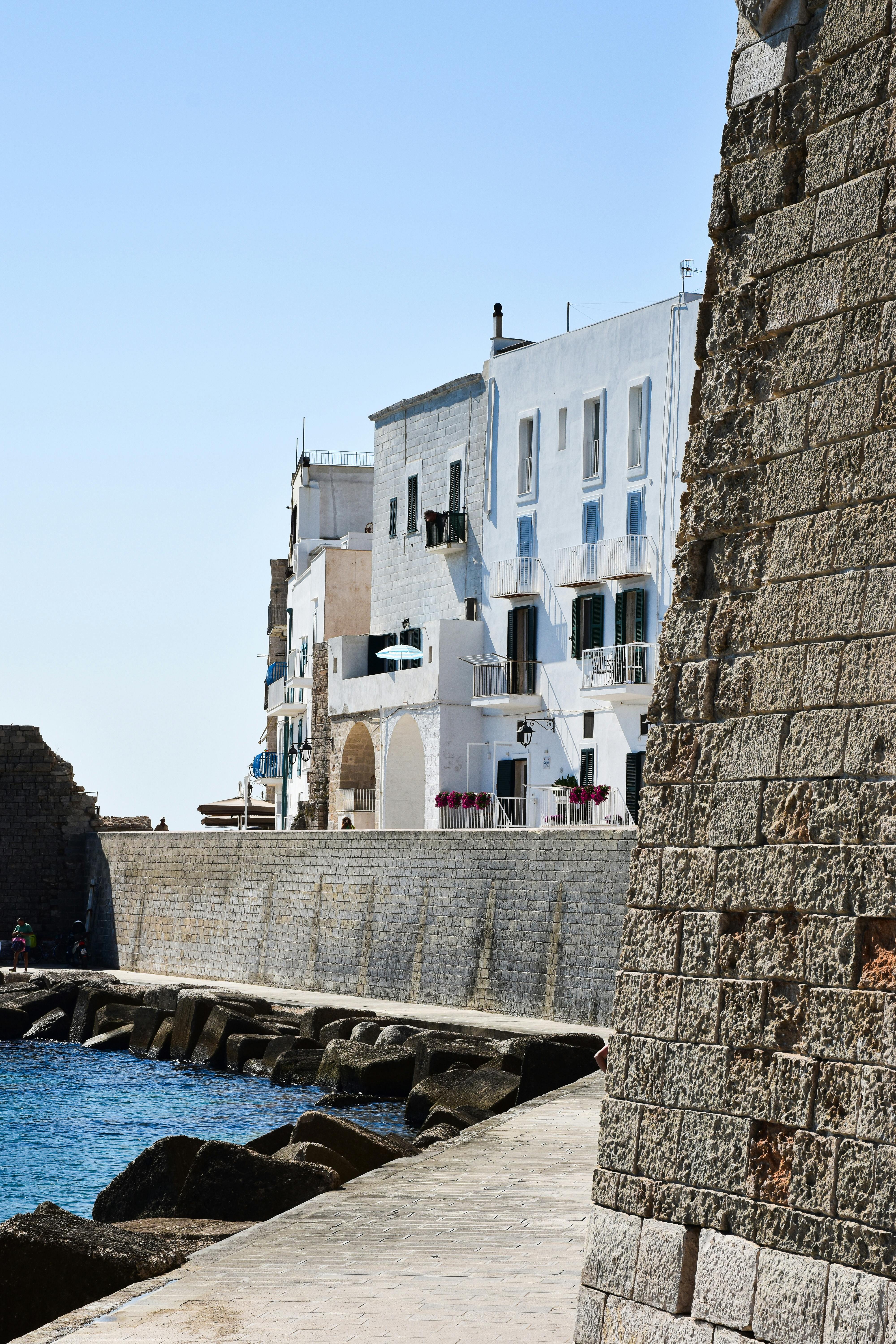 Azure blue sea water with white houses on a cliff during a sunny day and an old historical city wall.