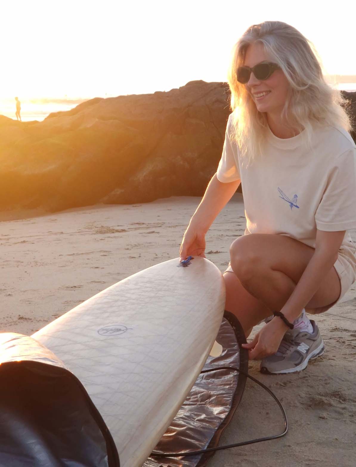 a blond women wearing a white t shirt taking out a surfboard from a case