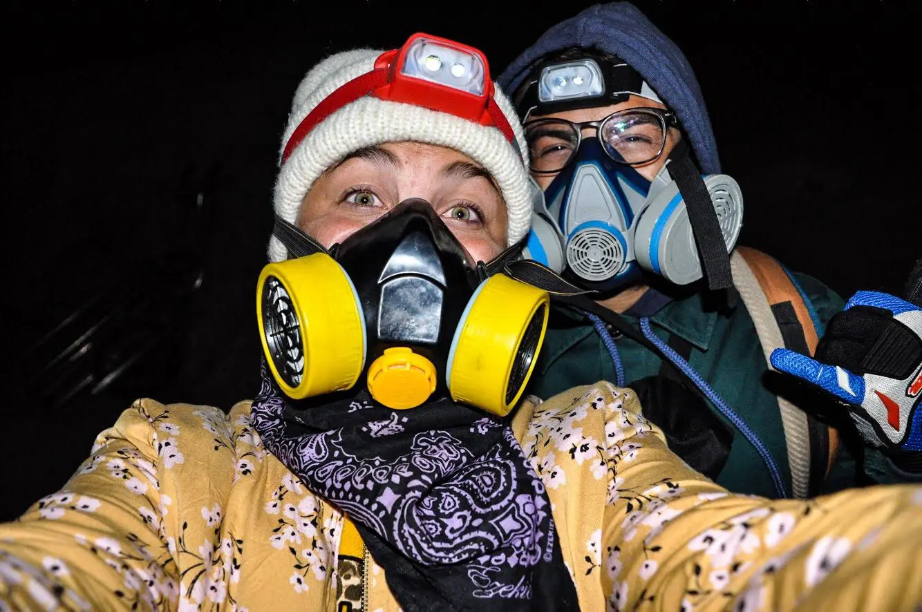 Deux personnes portant des masques à filtres et des lampes frontales, habillées chaudement, posant pour une photo de nuit.