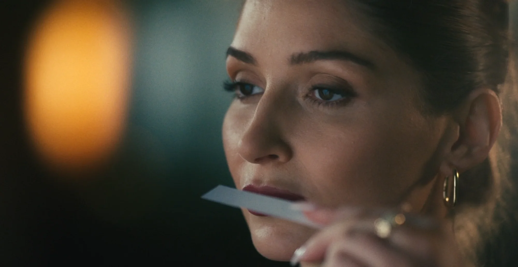 Woman smelling a perfume test strip in low warm light, from the Fraterworks film