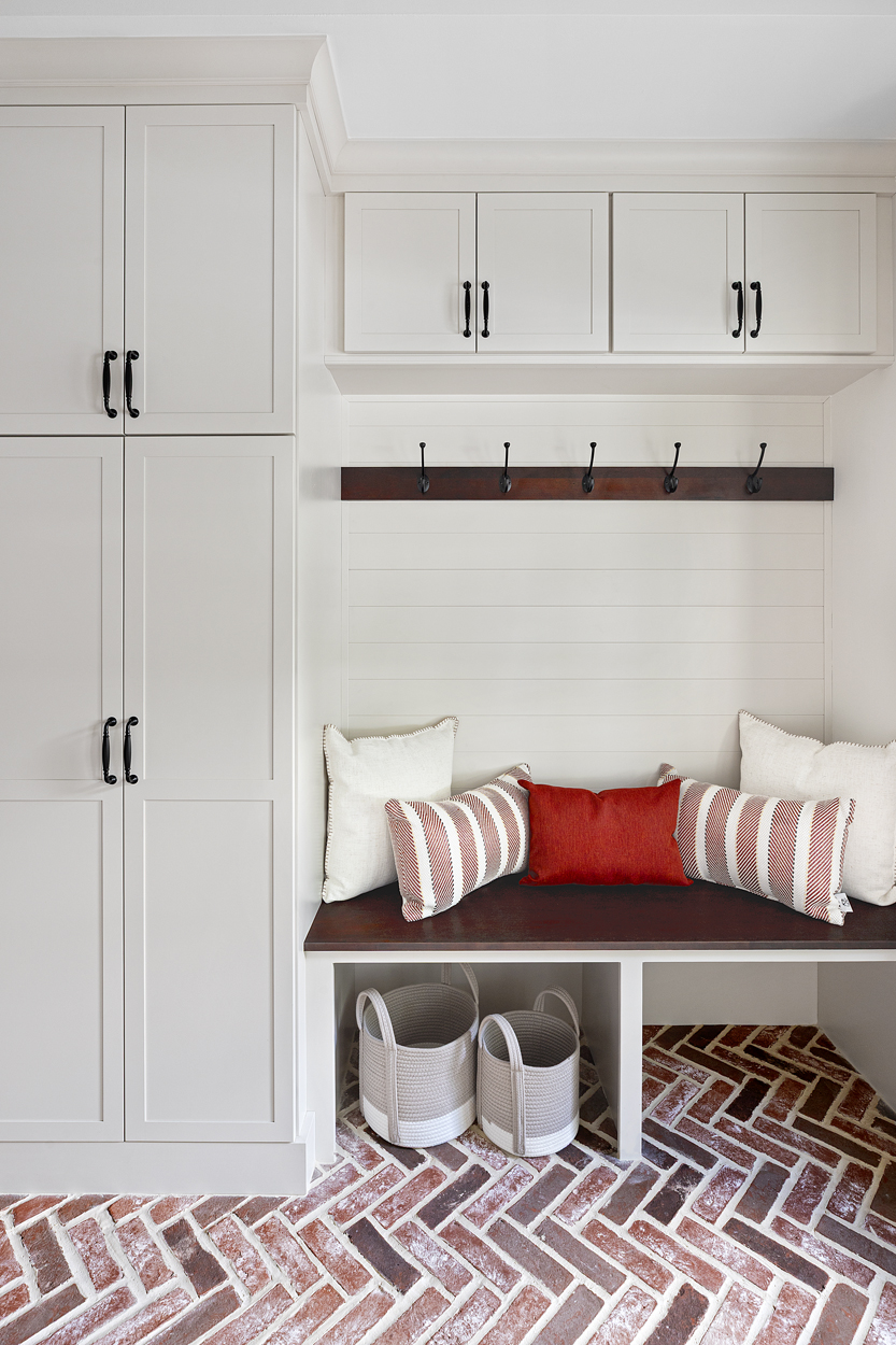The right side is dedicated to the full function of a mudroom, complete with a built-in bench, substantial cabinet storage fitted with custom shelving, dedicated coat closets, and upper cabinets that provide valuable additional space