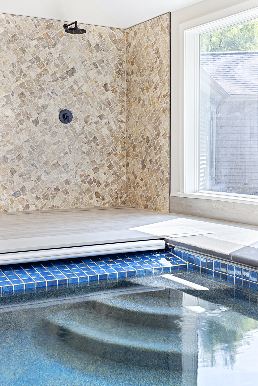  A shower wall clad in Broken Volcano Cobble Brushed Travertine creates an organic focal point, its natural texture and warm tones grounding the bright space