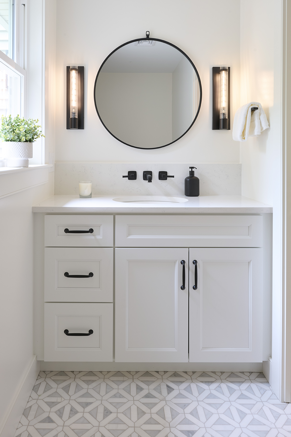 A round black-framed mirror anchored by geometric sconces commands attention above the Calacatta Vincenta quartz vanity