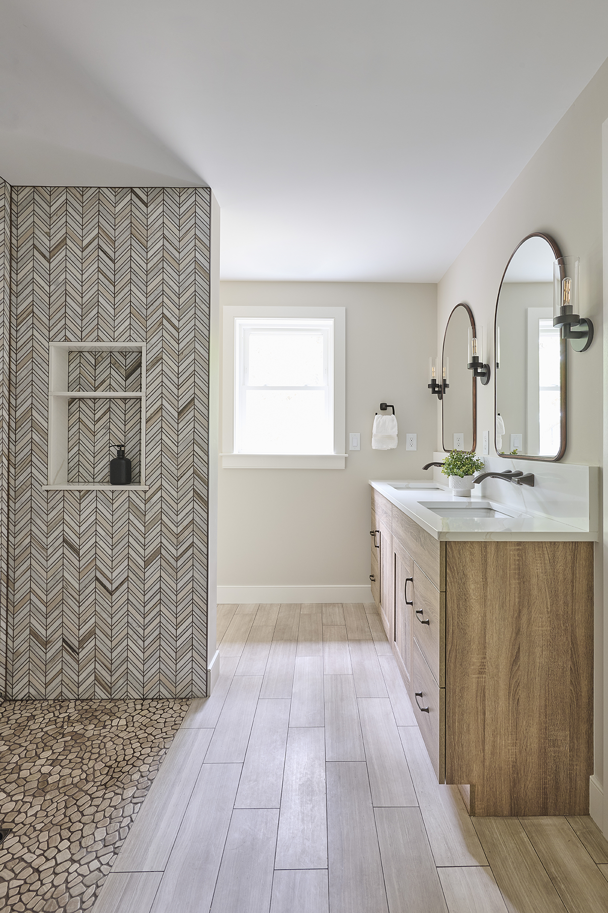 Lodge oak cabinetry anchors the dual vanity, while Palisandro marble chevron tiles create a striking focal wall in the walk-in shower