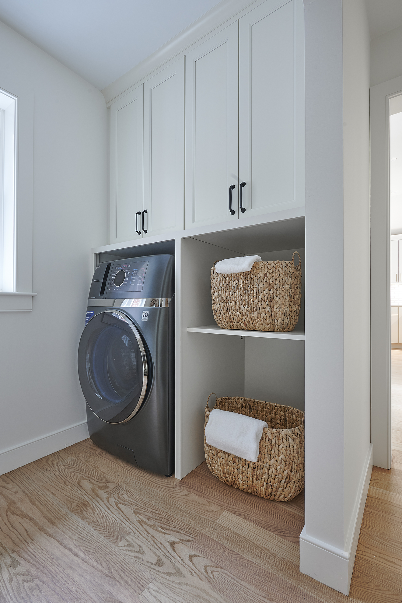 Extra: Woven baskets add warmth against crisp white walls and light wood flooring, proving functional spaces can be both practical and polished