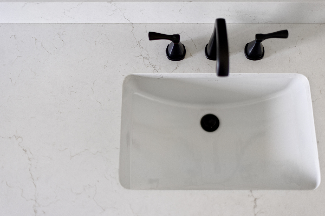 Softly veined quartz brightens the vanity surface while introducing a quiet layer of movement that plays beautifully against the patterned floor.