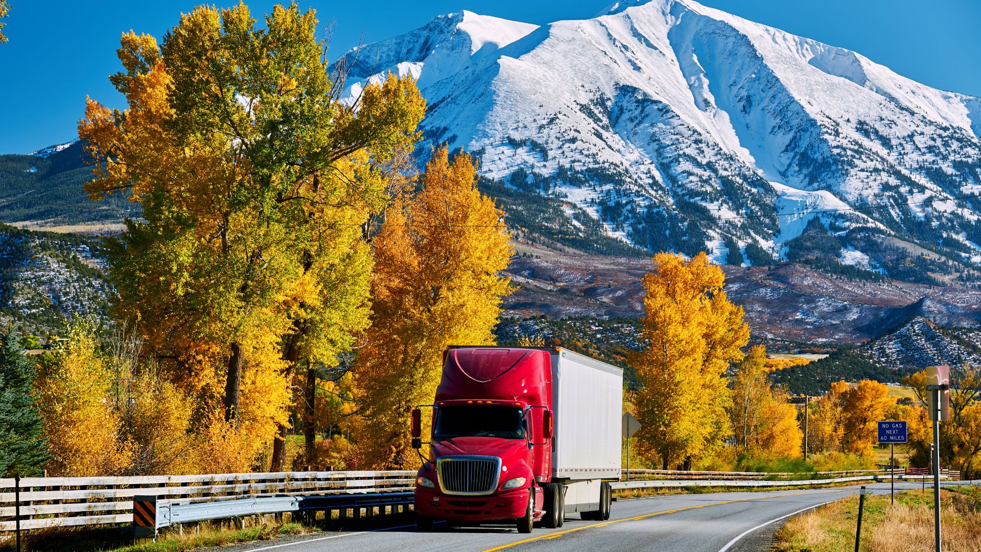 Red Semi Truck on a Highway with Snowy Mountains in the Background