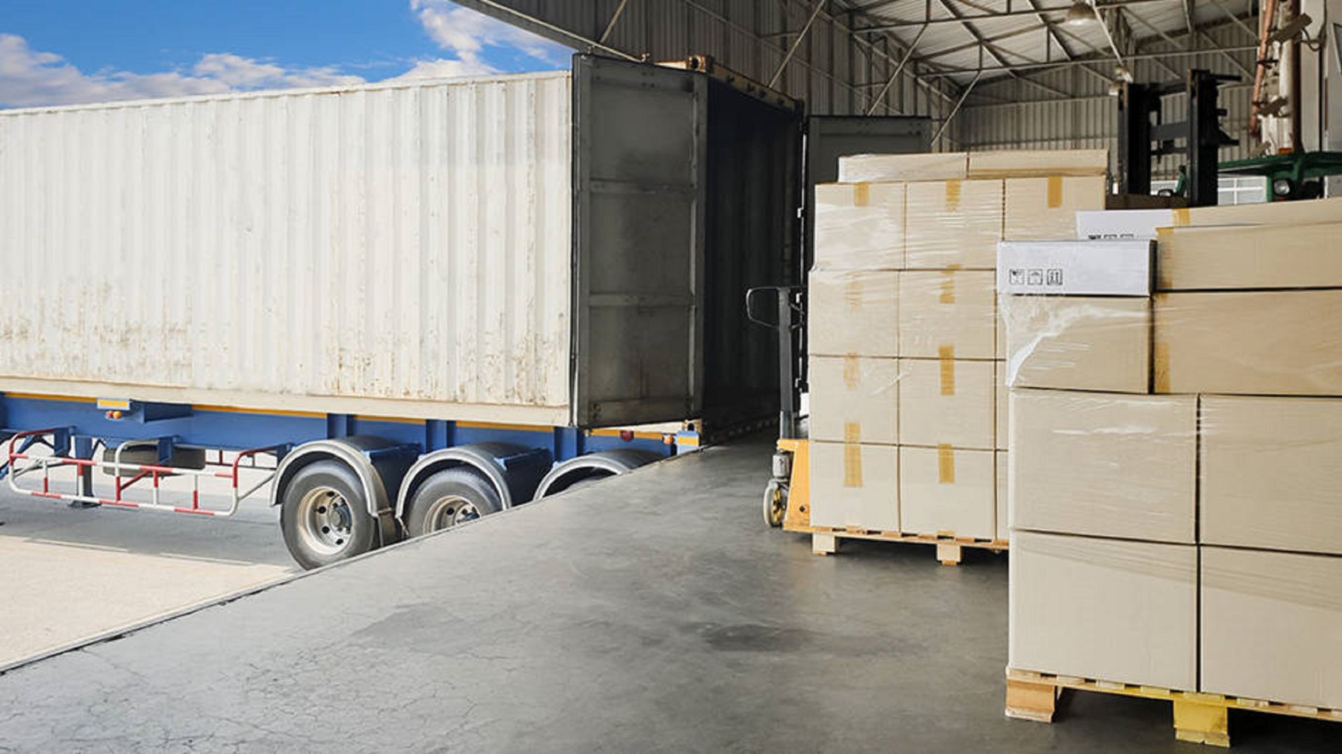 White Semi Truck at a Loading Dock Next to Pallets of Boxes