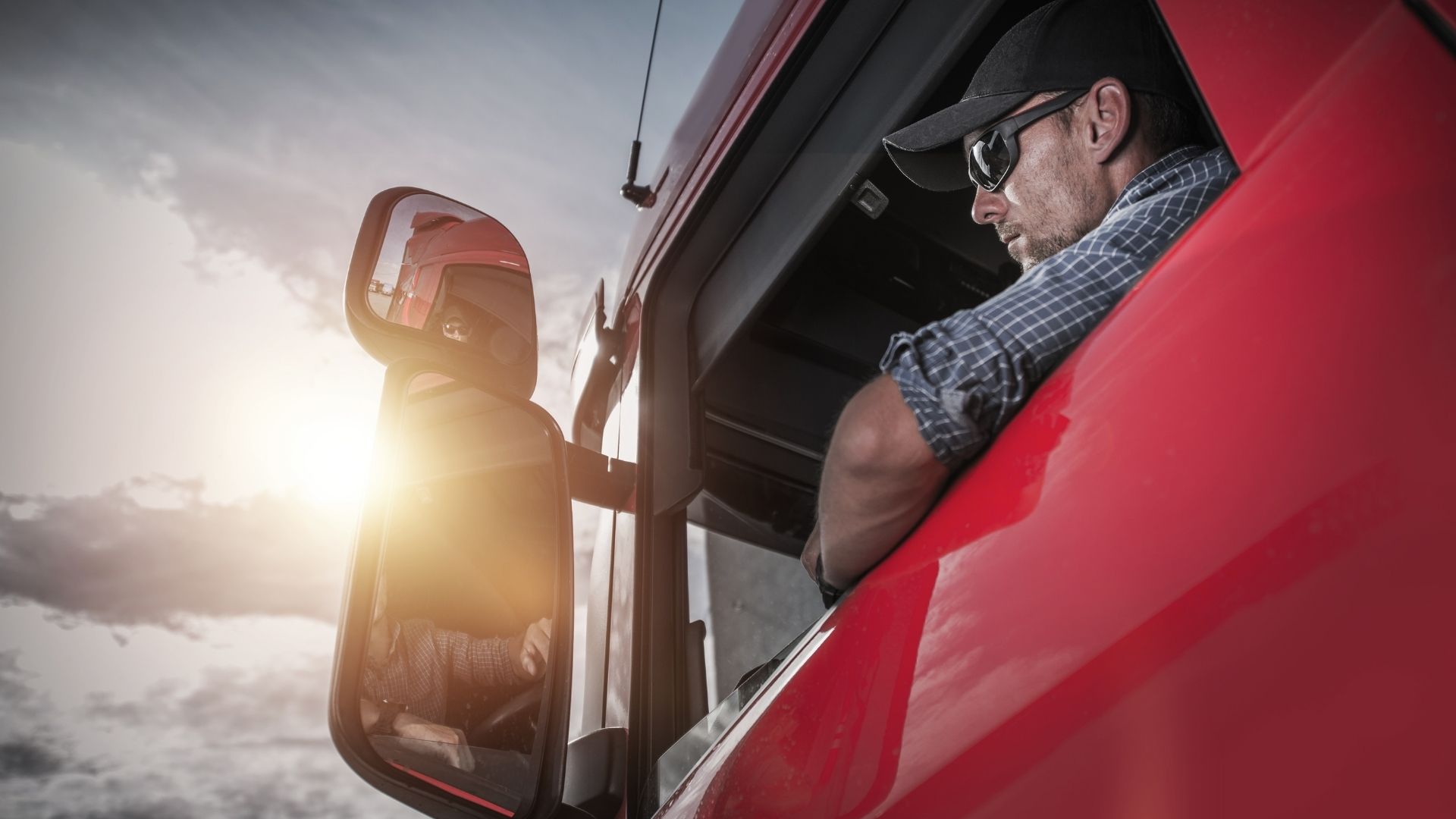 Man Behind the Wheel of Red Semi Truck with Sun Shining
