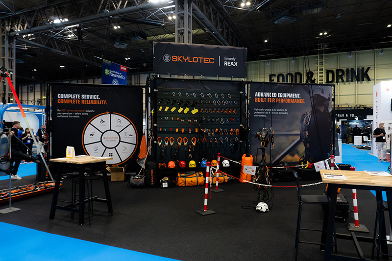 SKYLOTEC formerly REAX trade show booth displaying colorful safety gear and helmets on a pegboard, with banners highlighting equipment and service.
