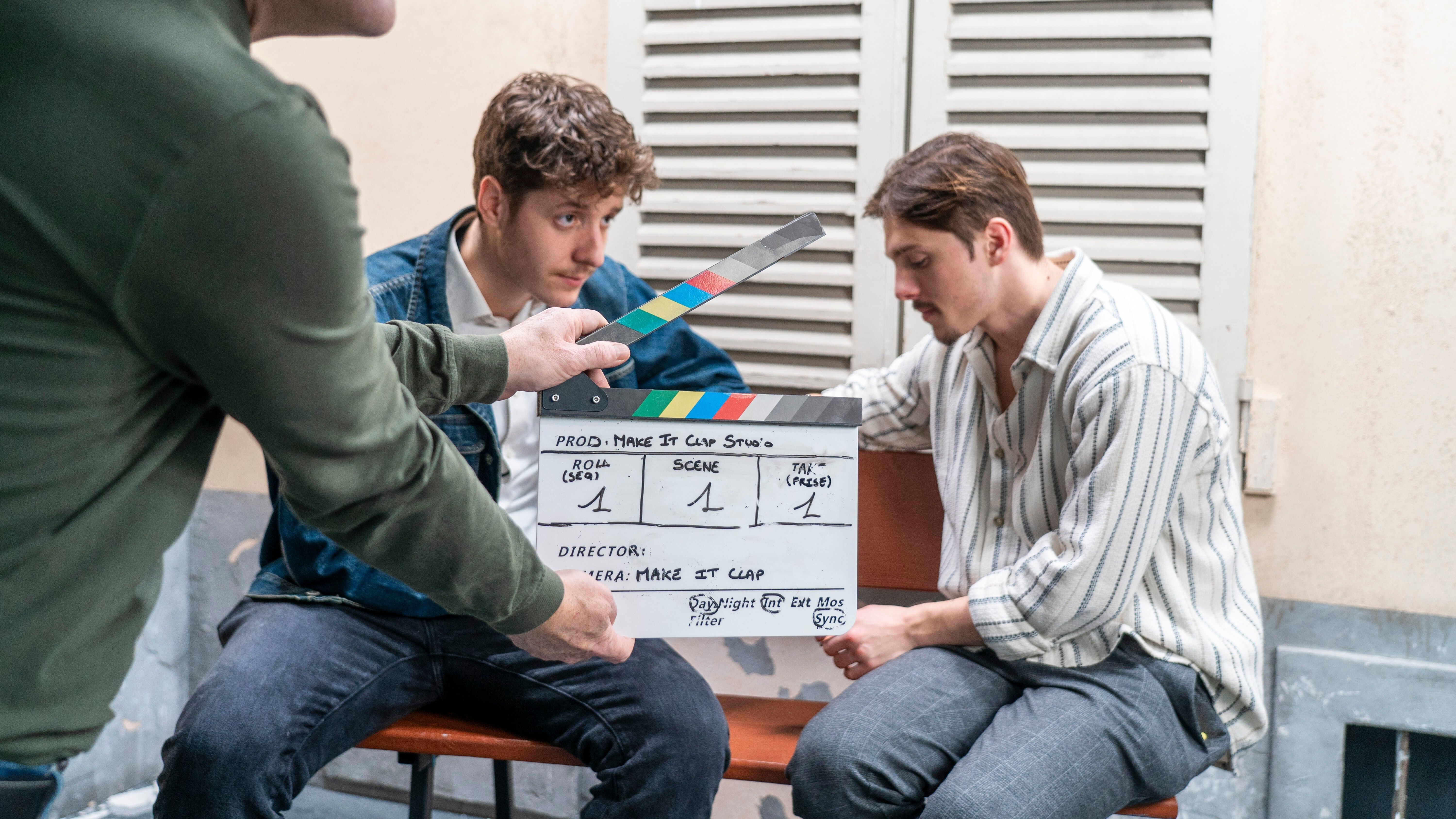 A clapperboard in front of two comedians ready to shoot a scene
