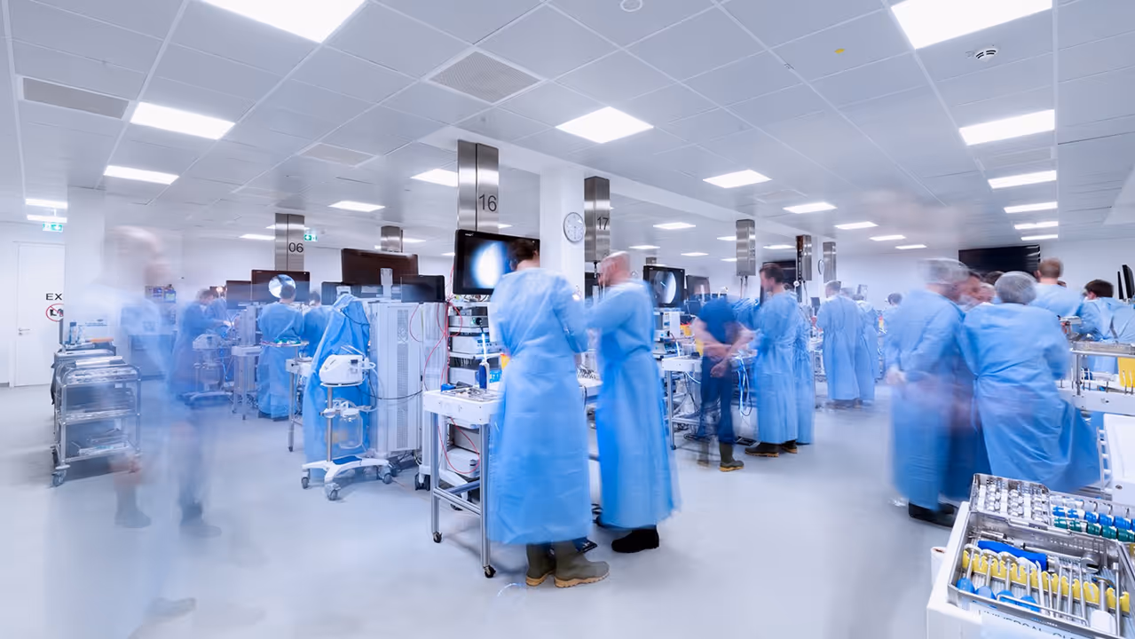 Many Arthrex surgeons stand at different training stations in a large, brightly lit room.