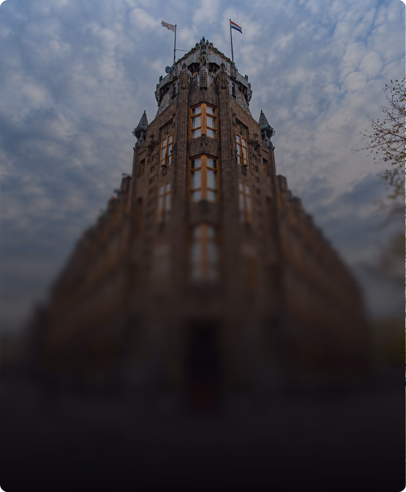 Symmetrically mirrored photo of a historic stone building with tall narrow windows, decorative architectural details near the roof, and flags atop the structure under a cloudy sky.