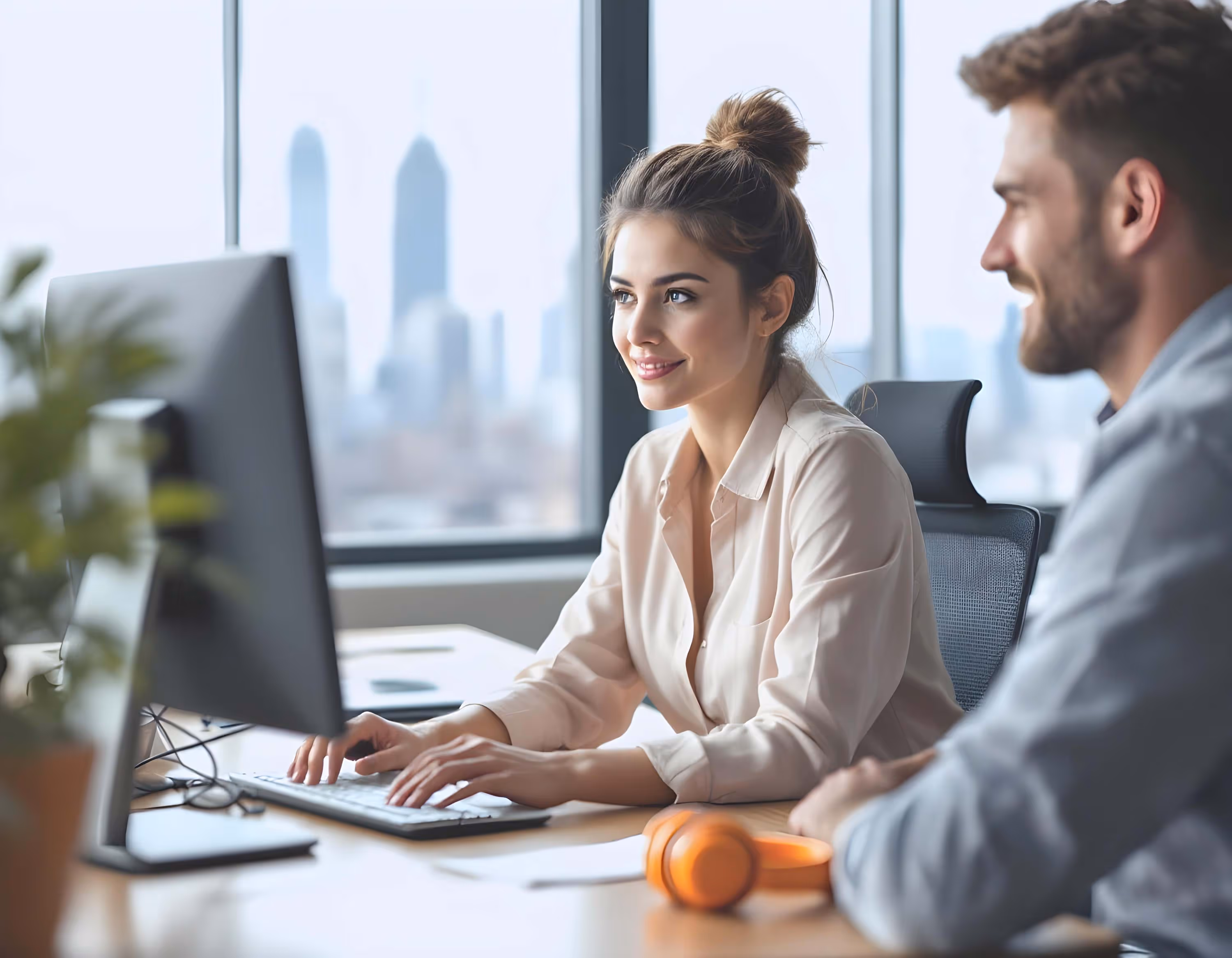 Zwei Personen in einem Büro sitzen vor einem Computer und arbeiten gemeinsam.