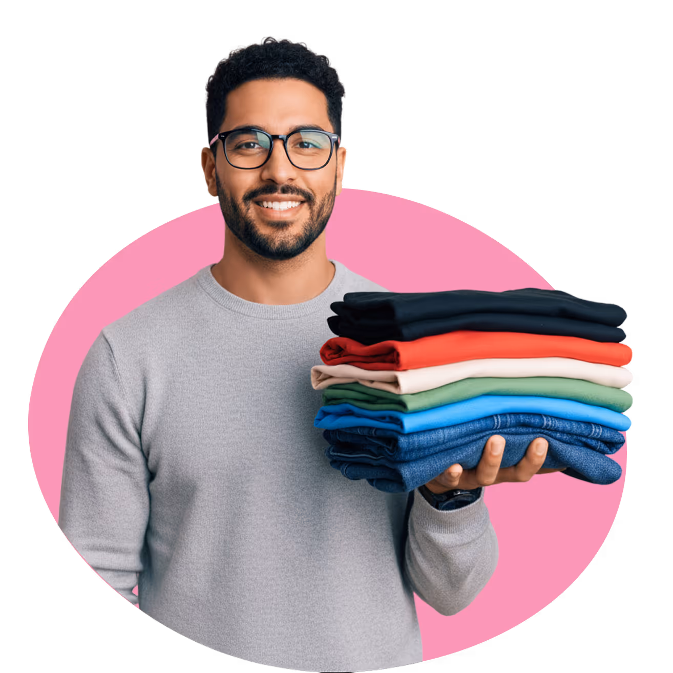 Hombre con gafas sonriendo y sosteniendo una pila de ropa doblada de varios colores frente a un fondo rosa.