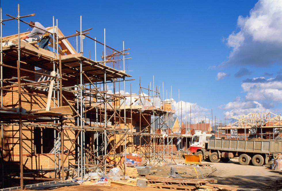 onstruction worker on scaffolding at a UK new-build housing site, illustrating delays in the planning and delivery pipeline